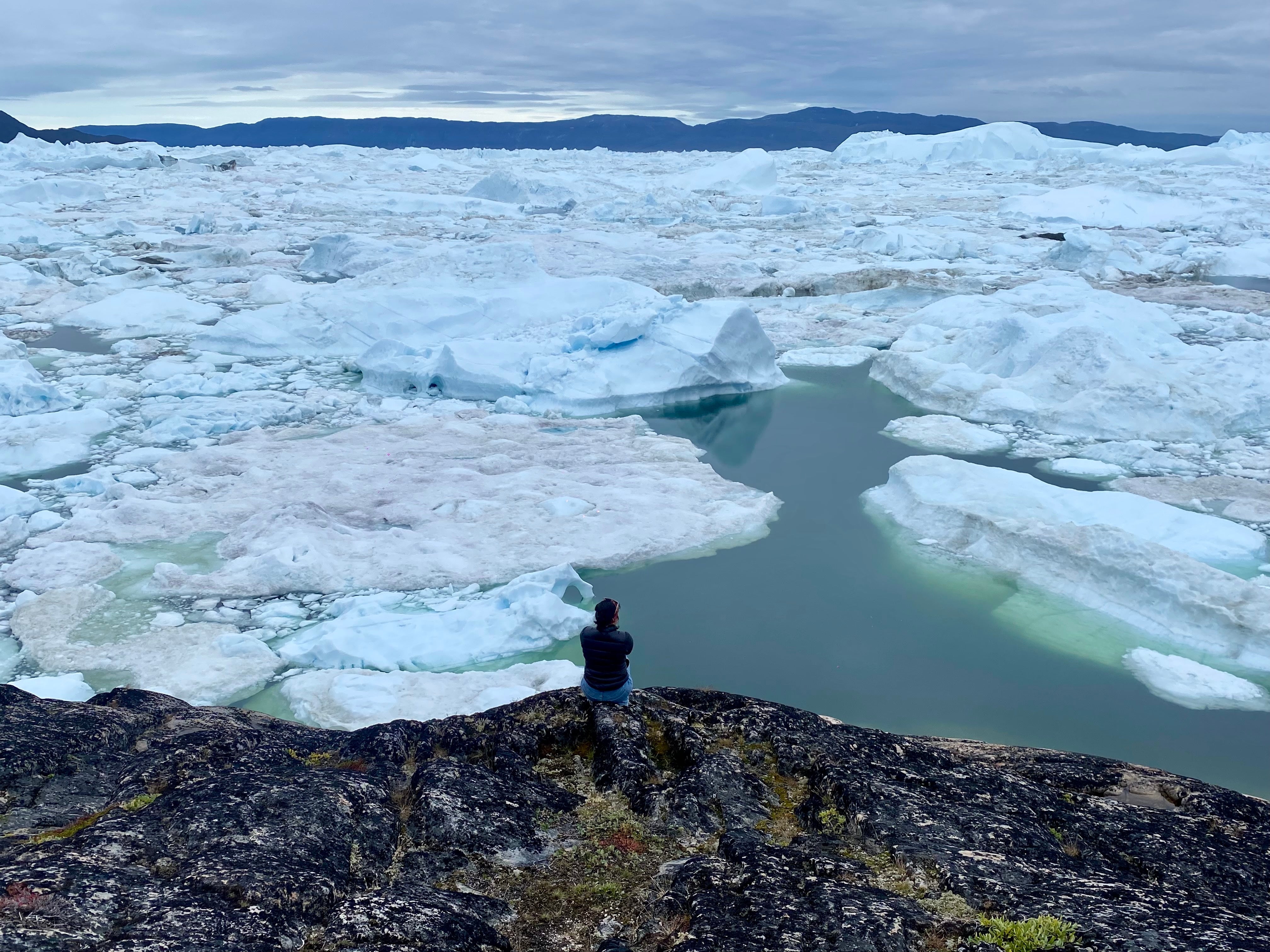 A woman sits alone overlooking a melting iceberg
